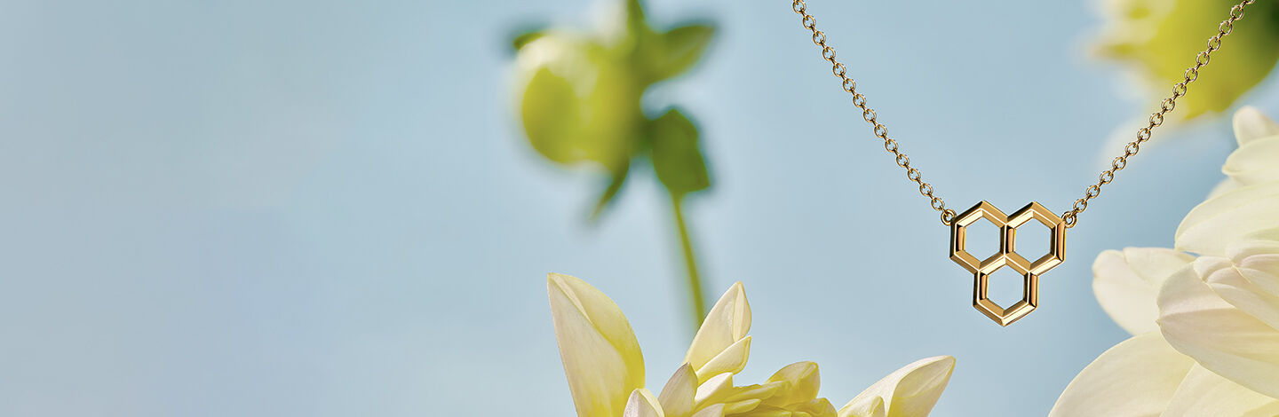 Birks Bee Chic gold honeycomb pendant resting on a floral and blue background.
