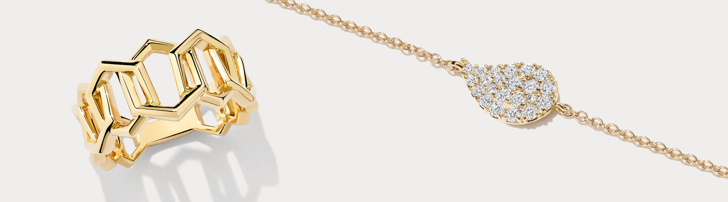 A Birks Bee Chic yellow gold ring and Birks Pétale yellow gold and diamond necklace on a greyish beige background.