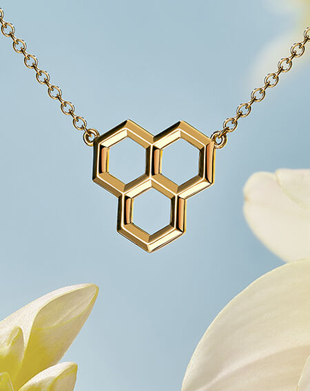 Pendentif Bee Chic en nid d'abeille doré sur fond de ciel avec une fleur blanche.