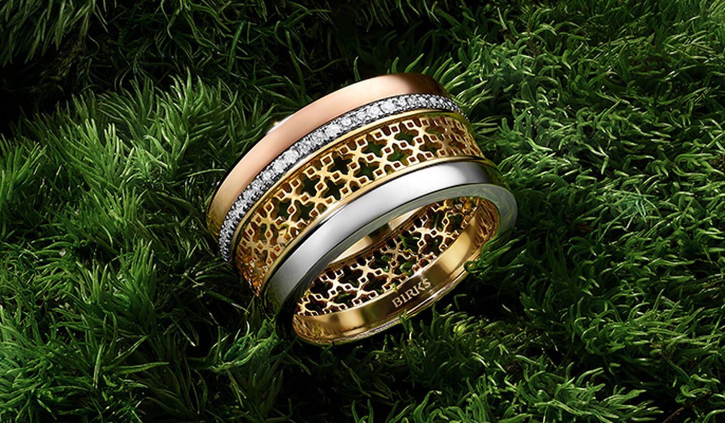 A Birks Dare to Dream tri-gold ring on a grassy background.
