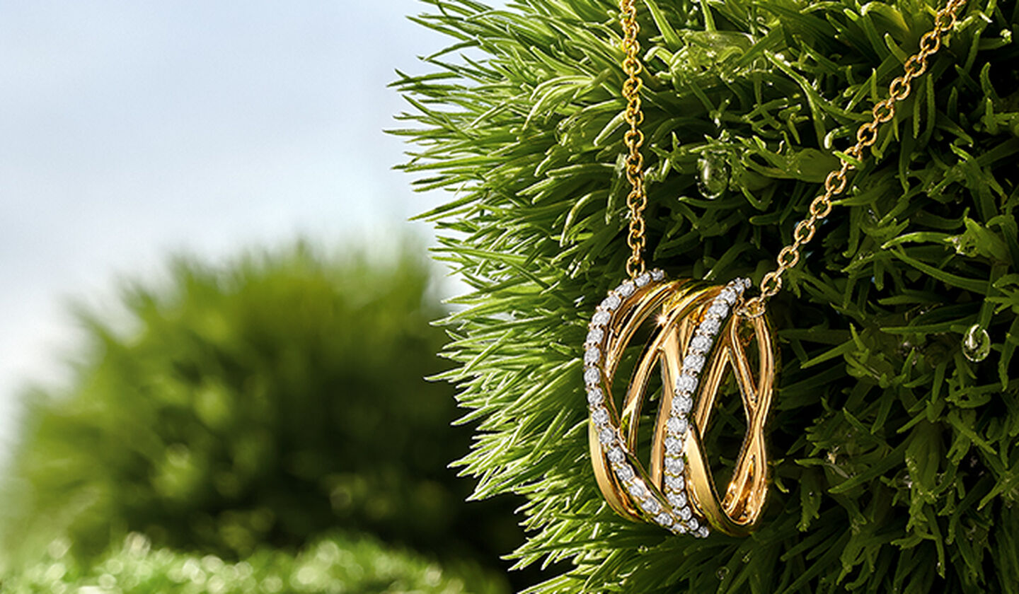 A yellow gold and diamond Rosée du Matin necklace on a green grass background.